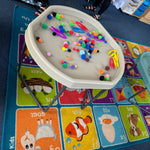 90cm plastic activity tables with gray metal legs in a classroom setting, filled with colorful toys and blocks, set on a colorful alphabet rug.